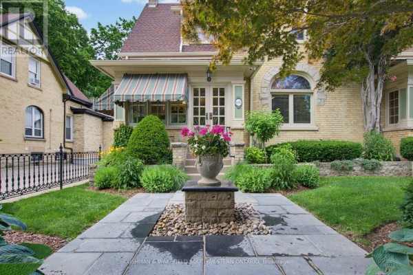 Pathway leading to the entrance of a yellow brick building with manicured bushes and flowers. - 602 Dufferin Avenue, London East