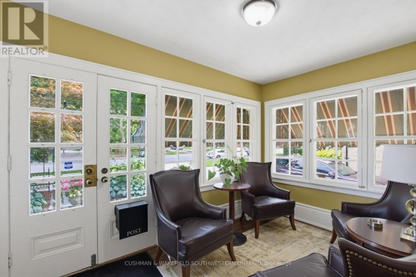 Interior seating area with leather chairs, a small table, and multiple windows overlooking greenery. - 602 Dufferin Avenue, London East