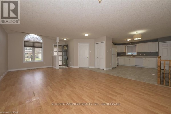 Open concept living room with light wood laminate flooring, leading to a kitchen area with white cabinets. - 602 Sprucewood Drive, London North