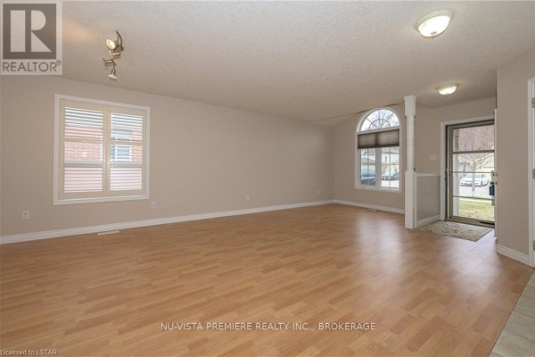 Spacious living room with light wood laminate flooring, large windows, and an entryway. - 602 Sprucewood Drive, London North