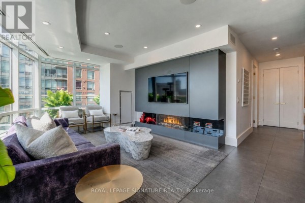 Living room with large windows, fireplace, modern sofa, and dual doors. - 602e - 500 Queens Quay W, Toronto