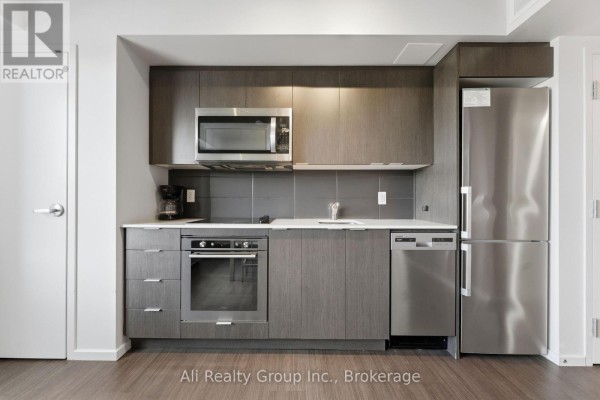 A modern apartment kitchen with dark wood cabinets, stainless steel appliances, and a gray tiled backsplash. - 603 - 105 Champagne Avenue S, Ottawa