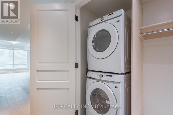 Stacked white front-loading washer and dryer in a closet with wooden shelves. - 603 - 1451 Wellington Street W, Ottawa