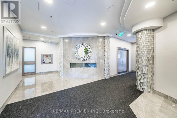 A building lobby featuring a modern fireplace, decorative wall art, and mosaic tile columns. - 603 - 200 Burnhamthorpe Road E, Mississauga