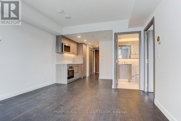 Living area adjacent to a kitchen and hallway, featuring dark wood floors and white walls. - 603 - 38 Widmer Street, Toronto