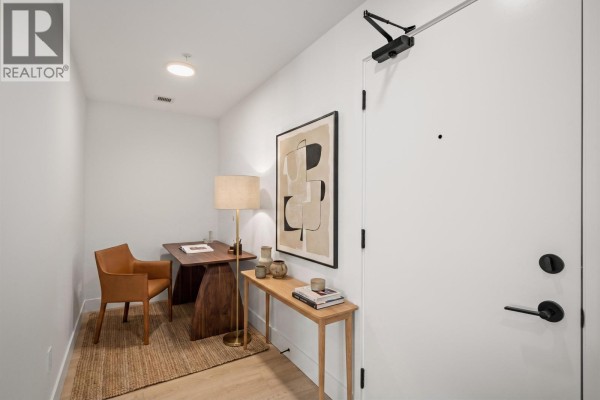 Small office area with a desk, chair, and a tall lamp next to the apartment entrance door. - 603 111 Buller Street, Port Moody