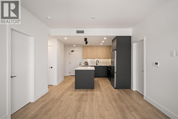 Open-concept kitchen and living area with a dark grey island, light wood cabinets, and stainless steel appliances. - 603 111 Buller Street, Port Moody
