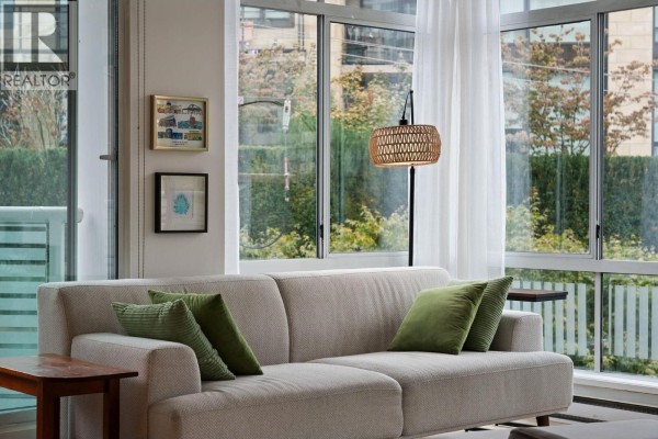 Close-up of a grey sofa with green cushions and a woven pendant lamp by the window. - 603 130 E 2nd Street, North Vancouver