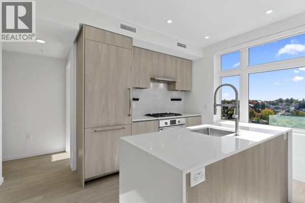 Modern kitchen with light wood cabinets, white countertops, and stainless steel appliances. - 603 3264 Vanness Street, Vancouver