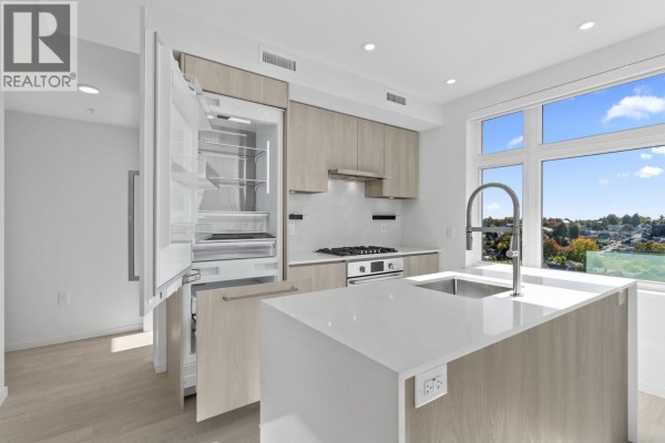 Open kitchen with light wood cabinetry, white quartz island, stainless steel appliances and large window. - 603 3264 Vanness Street, Vancouver
