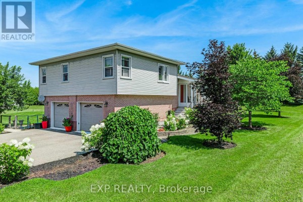 Front exterior of the house featuring a brick base, siding, a two-car garage, and surrounding greenery. - 6030 Doane Road, East Gwillimbury