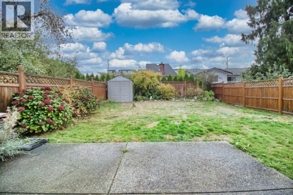 Rear yard with a concrete patio, green lawn, wooden fence, and a small shed. - 6031 Rumble, Burnaby
