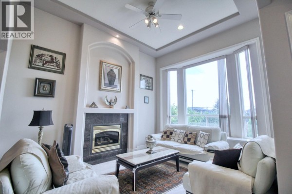 Living room with a gas fireplace, white sofas, coffee table, and a large bay window. - 6031 Rumble, Burnaby
