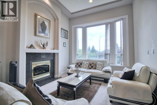 Living room features a dark marble fireplace surround, white seating, and a bay window view. - 6031 Rumble, Burnaby