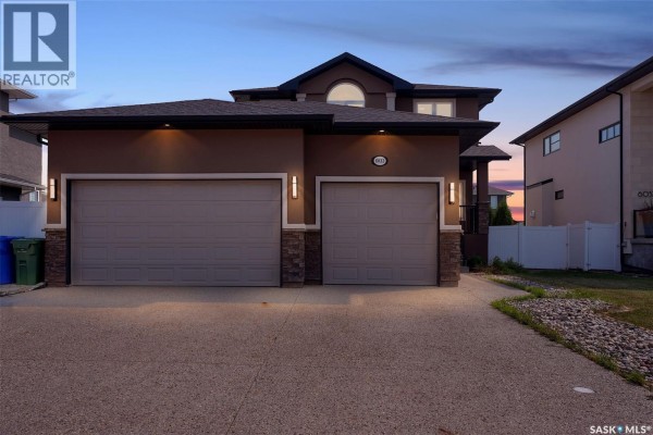 Front exterior of modern house with stucco siding and a two-car garage at dusk. - 6033 Little Pine Loop, Regina