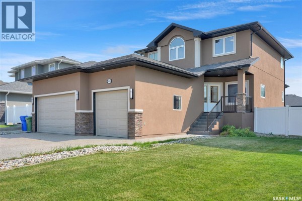 Side view of house with stucco siding, attached two-car garage, and green lawn. - 6033 Little Pine Loop, Regina