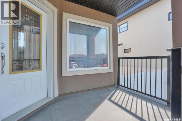 Close-up of front door and window on a covered porch with black metal railing. - 6033 Little Pine Loop, Regina