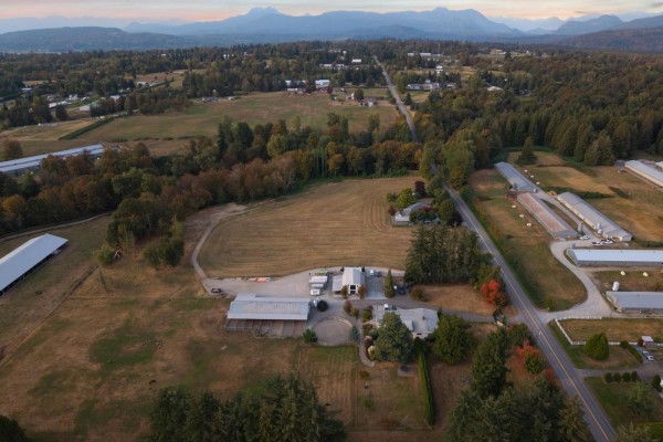Drone shot of farm buildings and surrounding land with mountains in the distance at dusk. - 6035 Bradner Road, Abbotsford