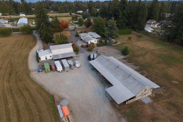 Close aerial view of farm structures including barns, trailers, and a riding arena. - 6035 Bradner Road, Abbotsford