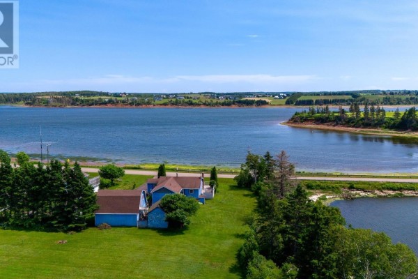 Aerial view of the blue house and surrounding property overlooking a wide bay and green fields. - 6036 Rte 20, Springbrook