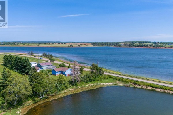 Aerial view of the blue house, outbuildings, and extensive waterfront property with a bay view. - 6036 Rte 20, Springbrook