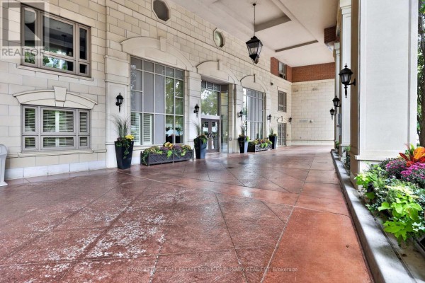 Covered entrance to an apartment building with stone facade, large windows, and planters. - 604 - 111 Forsythe Street, Oakville