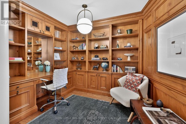 Home office with floor-to-ceiling wood paneled bookshelves, a desk, and a chair. - 604 - 111 Forsythe Street, Oakville