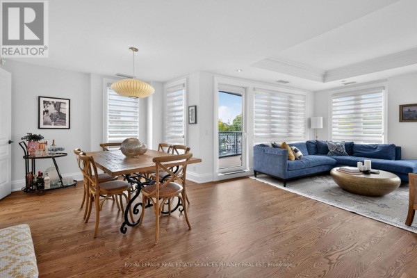 Living and dining area with a blue sectional sofa, wooden dining table, and a balcony view. - 604 - 111 Forsythe Street, Oakville