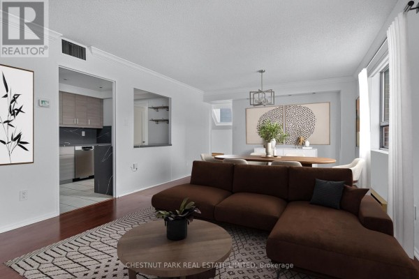 Open concept living and dining area with a brown sectional sofa, patterned rug, and view into the kitchen. - 604 - 19 Dundonald Street, Toronto