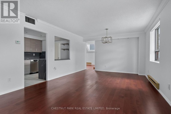 Living and dining area with dark hardwood floors and white walls, showing a modern chandelier and large windows. - 604 - 19 Dundonald Street, Toronto