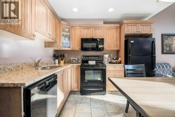 Kitchen with light wood cabinets, granite countertops, black appliances, and dining table. - 604 & 605, 401 4 Street, Rural Cypress County