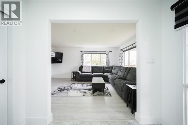 View through a doorway into a living room with a sectional sofa and large windows. - 604 Athabasca Avenue, Fort Mcmurray