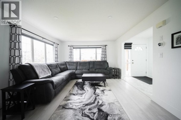 Living room with a large grey sectional sofa, black coffee table, and patterned rug. - 604 Athabasca Avenue, Fort Mcmurray