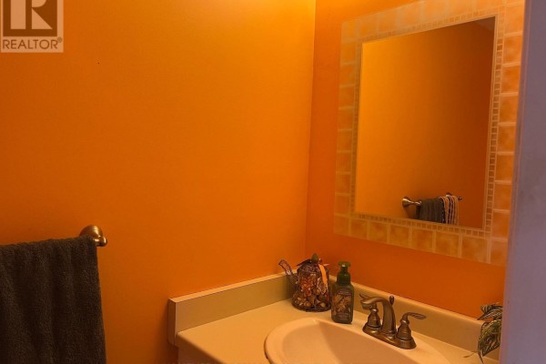 Powder room with a white vanity, a mosaic-tiled mirror, brass faucet, and bright orange walls. - 6043 Chidham Crescent, Mississauga