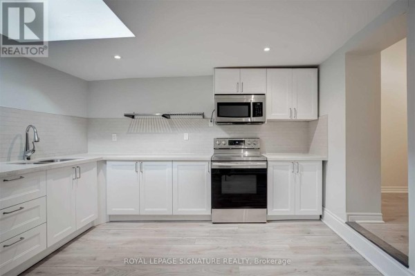 White kitchen with white cabinets, stainless steel appliances, and a skylight. - 604a Queen Street W, Toronto
