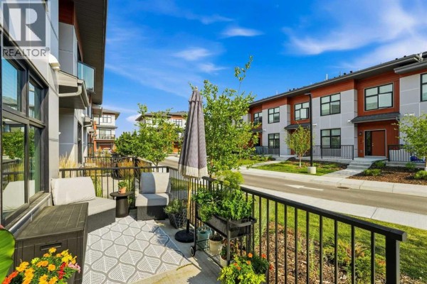 View from a townhouse balcony with seating, umbrellas, and potted plants overlooking a street. - 605, 400 Belmont Street Sw, Calgary