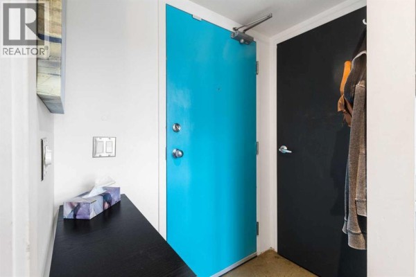 Interior view of a narrow hallway with a bright blue apartment door and a black door. - 605, 535 8 Avenue Se, Calgary