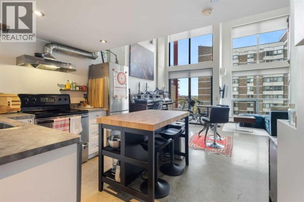Open concept kitchen and living area with concrete floors, stainless steel appliances, and large windows. - 605, 535 8 Avenue Se, Calgary