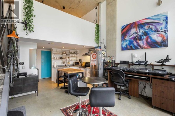 View of a loft apartment showing the kitchen, living area with DJ equipment, and a bicycle on the wall. - 605, 535 8 Avenue Se, Calgary