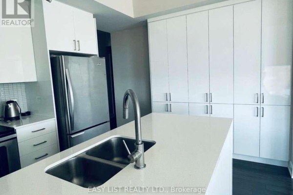 Modern kitchen with white cabinets, stainless steel refrigerator, and large island with sink. - 705 - 118 Holmwood Avenue, Ottawa