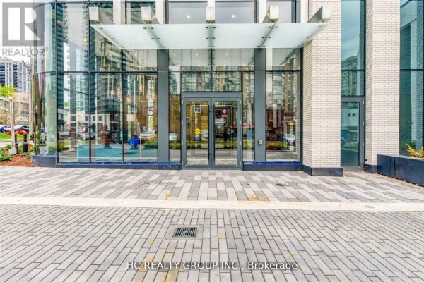 Glass entrance to a modern apartment building with patterned stone paving. - 605 - 15 Holmes Avenue, Toronto