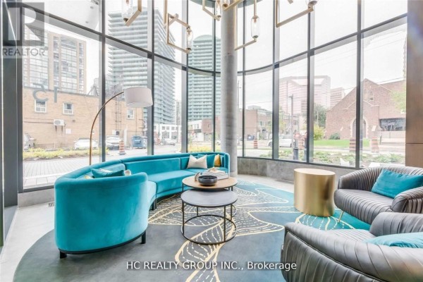 Lobby seating area with teal curved sofa, grey sofas, and round tables. - 605 - 15 Holmes Avenue, Toronto