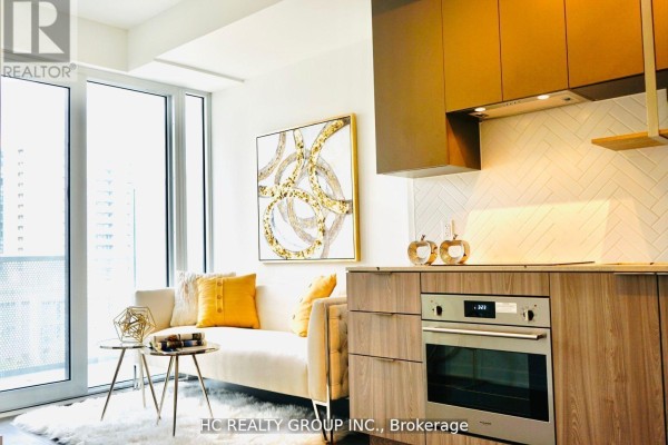 Living area with white sofa, gold abstract art, and wood-finish kitchen counter. - 605 - 15 Holmes Avenue, Toronto