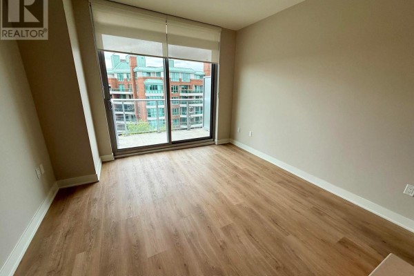 Empty room with hardwood floors and large window with balcony access overlooking buildings. - 605 - 275 Carling Avenue, Ottawa
