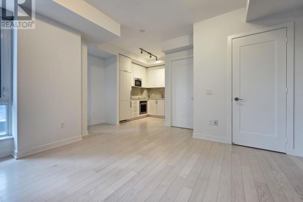 Open kitchen view with white cabinetry, stainless steel appliances, and light wood flooring. - 605 - 330 Richmond Street W, Toronto