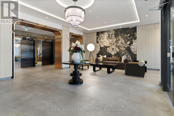 Building lobby with grey tile floors, modern furniture, and a large floral wallpaper accent wall. - 605 - 556 Marlee Avenue, Toronto