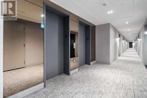 Hallway with grey carpet, textured walls, and a row of elevators with mirrored doors. - 605 - 556 Marlee Avenue, Toronto