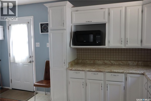 Kitchen cabinets, microwave, and tiled backsplash in a room with a light blue wall. - 605 5th Avenue W, Assiniboia