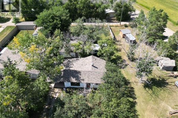 Aerial view of a single-story house with a dark roof, surrounded by mature trees and smaller outbuildings. - 605 Railway Avenue, Trochu