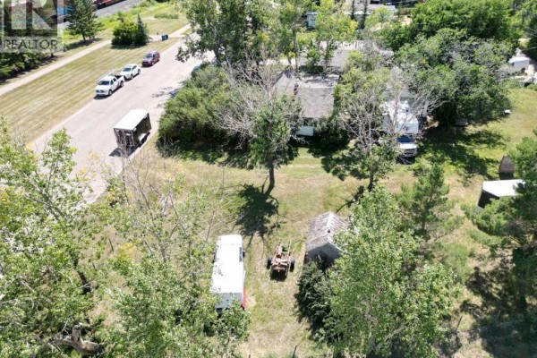 Aerial view of a property with a house, several outbuildings, trailers, and parked cars on a gravel road. - 605 Railway Avenue, Trochu